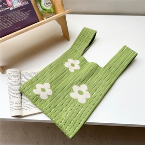 Detail of green knitted tote bag with white floral patterns in a cozy indoor setting