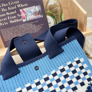 Detail of blue checkerboard knitted tote bag with snap closure on a wooden shelf