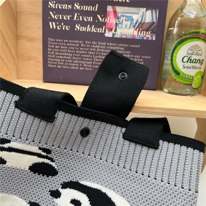 Close-up of a grey knitted tote bag featuring a black panda design and metal snap button