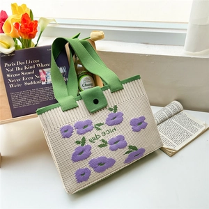 Detailed knit tote bag with purple flower patterns and green handles on a white desk