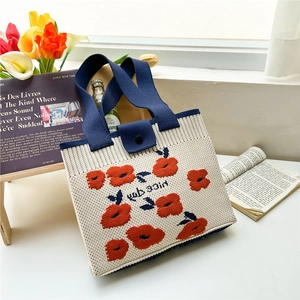Close-up of floral knit tote bag showing thick blue handles and secure button closure