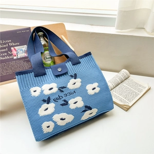Detail of blue knitted tote bag showing floral pattern and metallic button closure