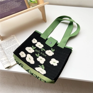 Close-up of black knitted tote bag featuring white floral patterns and green woven handles