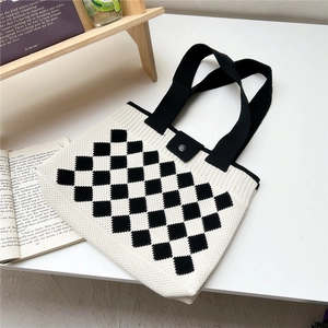 Detail of checkered knit tote bag showing black metal snap closure on white desk
