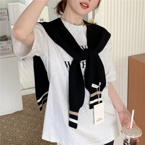 Detail of black knit shawl with brown and white striped cuffs worn over a grey T-shirt