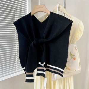 Detailed knit texture of a black V-neck shawl with retro stripe accents on a wooden hanger