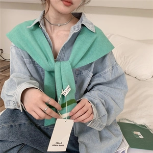 Close-up of mint green striped knit shawl draped over a blue denim shirt with tag