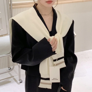 White knitted shoulder wrap with black stripes styled over a black blazer jacket