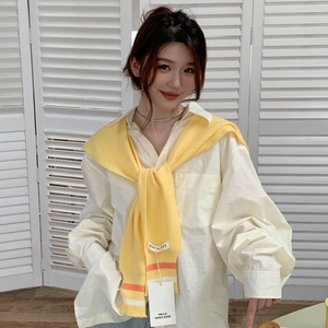 Detail of a yellow knitted shawl with striped edges over a white oversized shirt