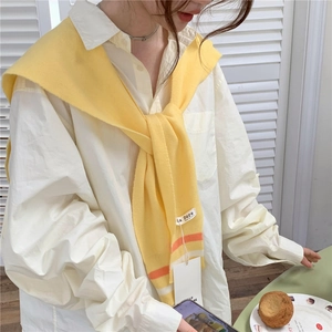 Detail of yellow knitted shawl wrap with orange and white striped trim on a white shirt