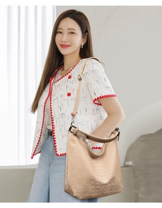 Beige crocodile embossed bucket bag shown as a shoulder bag on a model in daily outfit