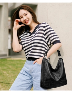 Outdoor lifestyle shot of a black croc-embossed hobo bag with wide shoulder strap detail