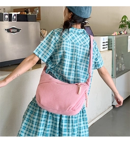 Detail view of pink corduroy crescent crossbody bag shown on model in cafe setting
