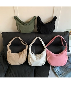 Detailed display of five colorful corduroy crescent crossbody bags on a black sofa