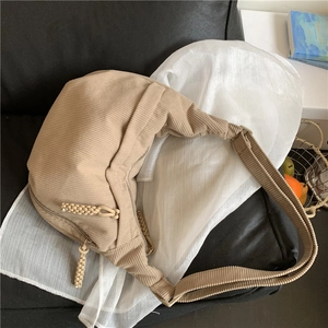 Beige corduroy crescent crossbody bag with adjustable strap on a cozy setup