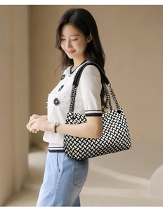 Détail d'un sac cabas tissé noir et blanc avec bandoulière chaîne sur l'épaule
