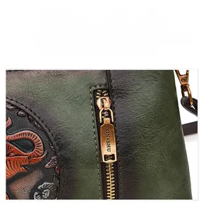 Close-up of vintage dark green leather bag featuring embossed floral detail and bronze zipper