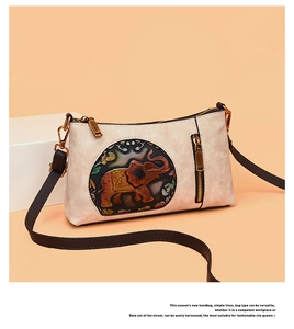 Detail of cream leather shoulder bag featuring ethnic elephant embossed design and gold zip