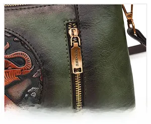 Detail of dark green pebbled leather bag featuring elephant embossing and golden metal zipper