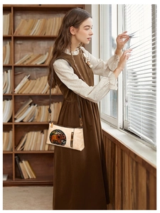 Detail of beige crossbody bag featuring orange elephant embroidery in a retro library