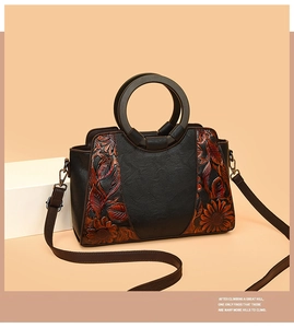 Close-up of vintage floral embossed patterns on black leather handbag with wooden handles