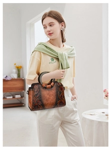 Detail of vintage brown leather bag with floral embossing and round wooden handle
