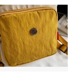Détail du sac bandoulière en nylon jaune froissé avec logo en métal et sangle