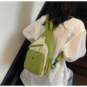 Détail du sac bandoulière en nylon vert et blanc avec logo en métal rond et poches zippées