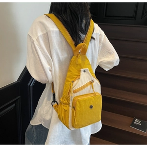 Détail d'un sac à dos en nylon jaune et crème porté par un mannequin dans un escalier