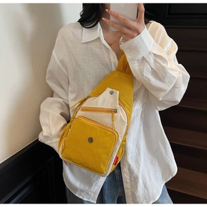 Détail du sac de poitrine en toile jaune et beige avec poches zippées et logo métallique