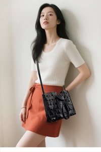 Detail of black laser-cut hollow pattern handbag styled with a white and orange outfit