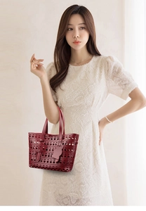 Detail of burgundy hollow-out leather tote bag held by a model in a white dress