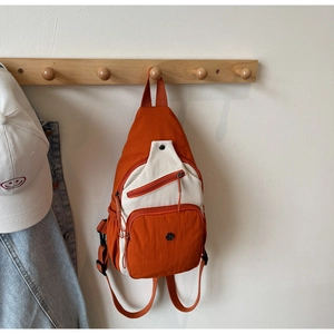 Détail d'un sac bandoulière fonctionnel orange et crème suspendu à un portant en bois