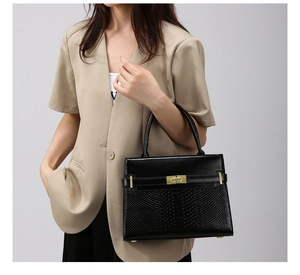 Close-up of black handbag featuring crocodile embossed leather and a gold turn-lock