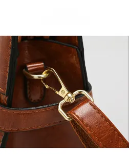 Detail of reddish-brown vintage leather bag featuring golden lobster clasp and adjustable strap