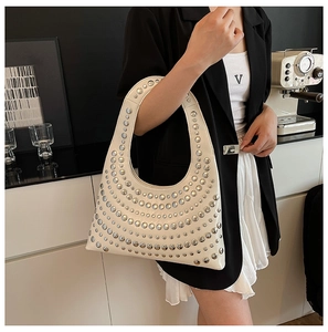 Detail einer beigen Hobo-Tasche mit silbernen Nieten, getragen von einem Model im Raum