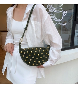 Dark green suede crescent bag with gold rivets shown worn as a stylish shoulder bag