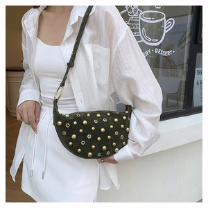 Macro detail of dark green suede crescent bag with gold studs and grommet accents