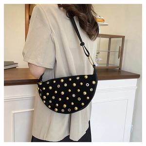 Detail of black suede crescent bag featuring golden rivets and metal eyelets on strap