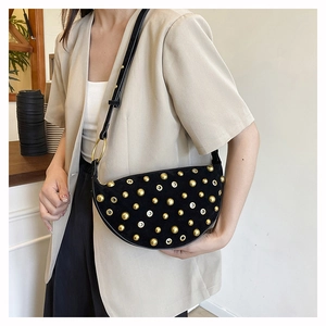 Detail view of black suede crescent bag with gold studs and rings on a model