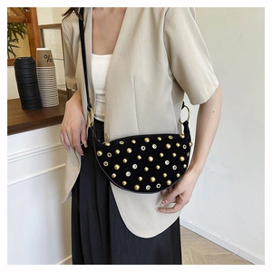 Detail of black suede punk style saddle bag with gold rivets worn on model shoulder
