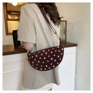 Close-up of wine red suede crescent bag with gold stud detailing and metal eyelets
