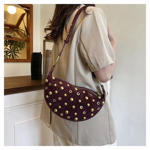 Gros plan du sac demi-lune en daim bordeaux avec clous dorés porté par un mannequin