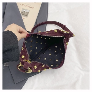 Gros plan d'un sac en daim bordeaux avec rivets dorés et finitions métalliques de qualité