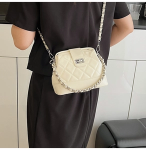 Dettaglio borsa trapuntata crema con catena e chiusura a girello indossata da modella