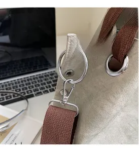 Detail of high-gloss silver hardware and brown woven strap on canvas tote bag