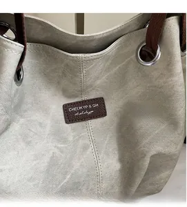 Detail of grey canvas tote bag showing twill texture and brown leather logo patch