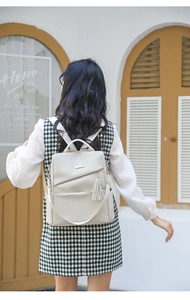 Detail eines cremeweißen Lederrucksacks mit Litschi-Struktur, Quasten und Metallbeschlägen