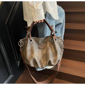 Dettaglio borsa tote vintage grigia con rivetti e manici in pelle marrone su scale in legno