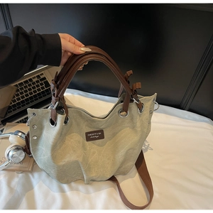 Dettaglio della borsa tote in tela verde salvia con manici in pelle marrone e rivetti